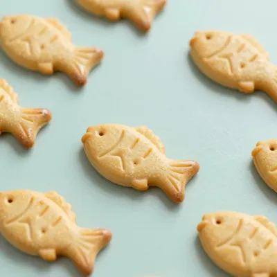 Golden Fish-Shaped Crackers on Light Blue Background - Food - AI generated image