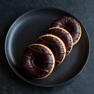 Chocolate Donuts with Red Drizzle on Black Plate - Food - AI generated image